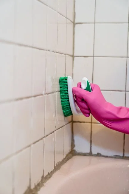 Anonymous person washing golden shiny faucet and sink in bathroom while wearing yellow latex glove during household care routine work